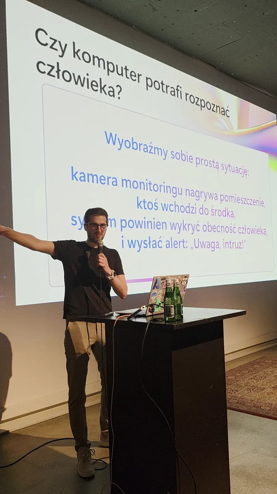 Marcin Gąstół na scenie, slajd „Czy komputer potrafi rozpoznać człowieka?”